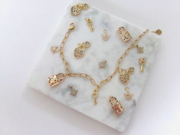 Sparkly gold charm bracelet flatlay on a white marble slab featuring heart-shaped locks, tiny keys, decorative padlocks and star charms studded with multicolored crystals