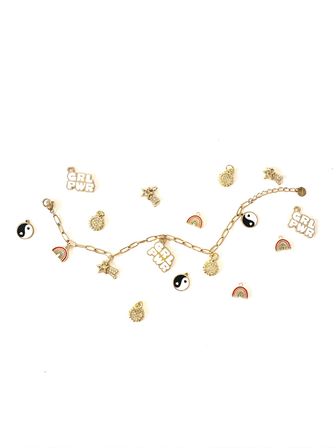 Playful gold charm bracelet flat lay on white background featuring GRL PWR text charms, yin-yang discs, tiny rainbow enamel charms and sparkling sunburst and star charms.