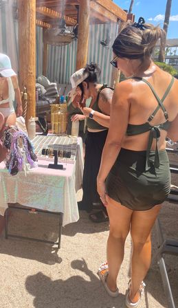 Sunny poolside cabana pop-up at a resort with guests browsing gold necklaces, bracelets and colorful scarves on a vendor table under a wooden pergola