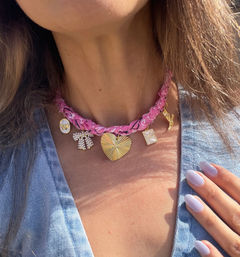 Close-up of a pink braided choker with gold heart and mixed charm pendants worn on a woman's neck, paired with lavender almond-shaped nails and a light denim top.