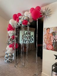 Indoor home doorway decorated with a pink, white and silver balloon arch with cow-print balloons, a spiky silver star and long metallic fringe streamers for a party entrance.