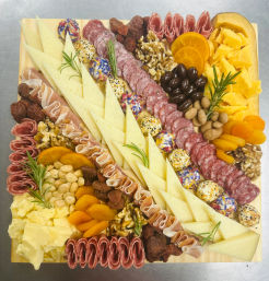 Square wooden charcuterie board with triangle-sliced cheeses, rolled salami and prosciutto, cheddar chunks, herbed cheese balls, mixed nuts, olives, dried apricots and rosemary — elegant appetizer grazing board