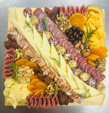 Square wooden charcuterie board with triangle-sliced cheeses, rolled salami and prosciutto, cheddar chunks, herbed cheese balls, mixed nuts, olives, dried apricots and rosemary — elegant appetizer grazing board