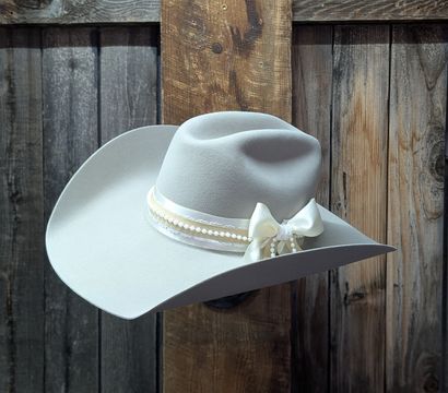 Cream felt cowboy hat with ivory ribbon, pearl trim and bow displayed against a rustic barn-wood backdrop