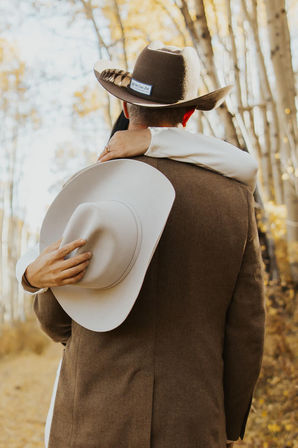 Romantic couple embracing in a golden aspen grove, man in a brown jacket and cowboy hat while the partner holds a white hat behind him.