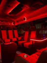 Luxury party van interior with red LED ambient lighting, diamond-quilted leather seats, illuminated side table and cup holders, and a starry fiber-optic ceiling.