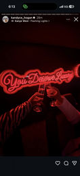 Two hands clinking champagne flutes beneath a red neon sign reading "You Deserve Luxury" in a dim, neon-lit lounge