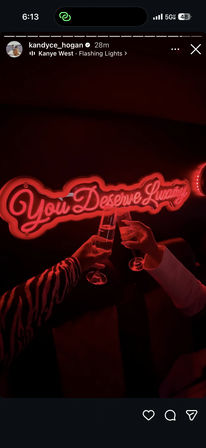 Two hands clinking champagne flutes beneath a red neon sign reading "You Deserve Luxury" in a dim, neon-lit lounge