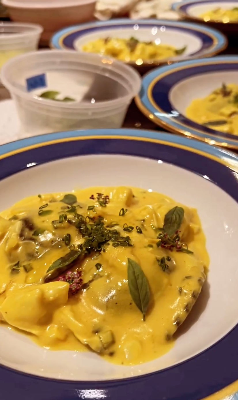 Creamy saffron-colored pasta in a blue-rimmed bowl, topped with fresh basil leaves and microherbs — elegant Italian-style plating