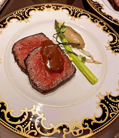 Gourmet medium-rare seared beef medallions with glossy brown sauce, asparagus spear and puree on an ornate gold-rimmed fine-dining plate