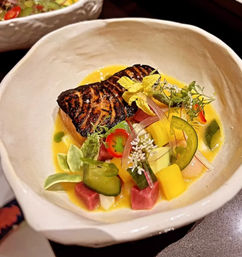 Seared glazed salmon fillet in a modern ceramic bowl on a bright mango-citrus sauce, garnished with cucumber slices, mango and pickled vegetable cubes, red chili, edible flowers and microgreens — elegant restaurant plating.