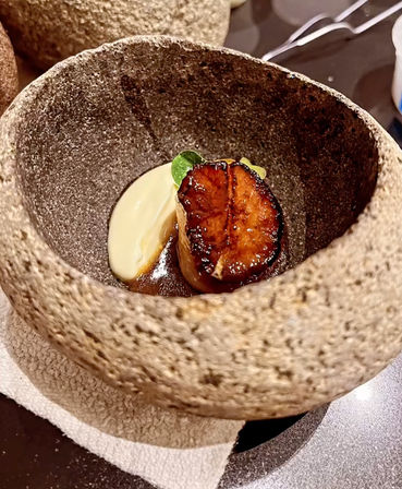 Seared caramelized scallop on a silky creamy purée with brown sauce and a microgreen, plated in a textured stone bowl — rustic-chic fine-dining dish.