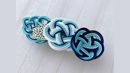 Teal, mint and navy braided cord knot accessory in mizuhiki style on a pale wood background