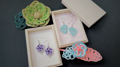 Colorful handmade mizuhiki knot earrings and braided cord accessories in pastel teal, coral, purple and green displayed in wooden gift boxes on a dark background