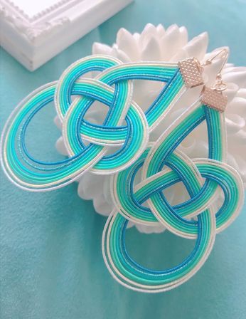 Ocean-inspired turquoise, teal and white knotted cord earrings with gold hooks – intricate looped mizuhiki-style design on an aqua background