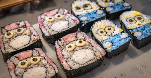 Colorful Japanese-style decorative sushi rolls shaped like cute cartoon animal faces with pink and blue rice, nori outlines and egg-and-seaweed eyes