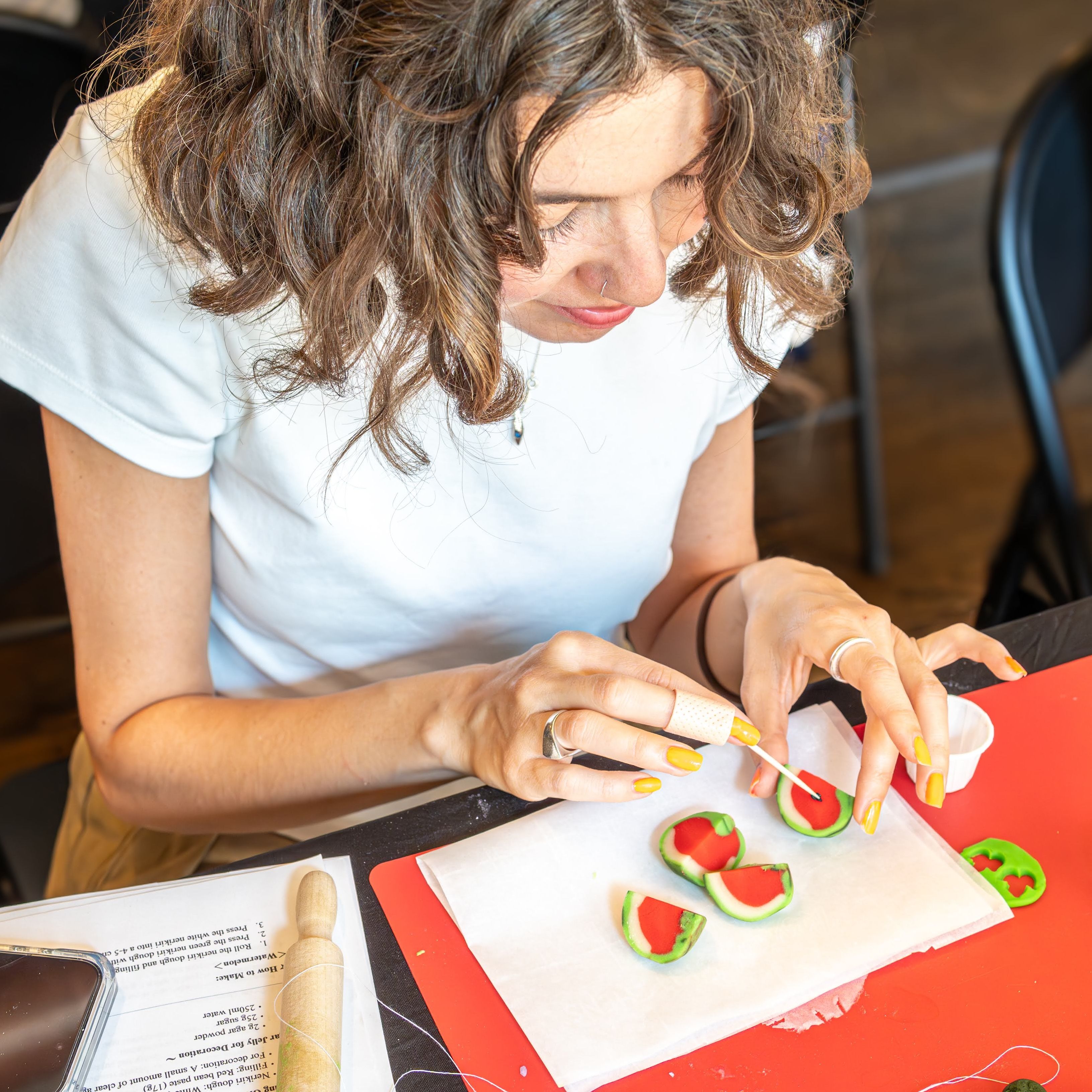 Person with curly hair decorating miniature green-and-red watermelon slices (clay or fondant) on a red craft mat