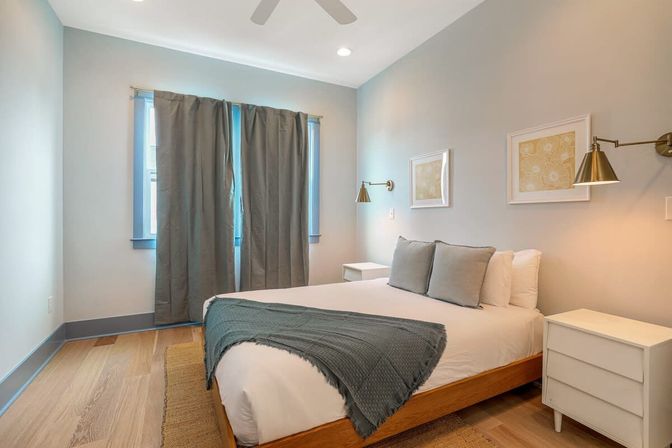 Cozy modern minimalist bedroom with queen bed, gray throw and pillows, white nightstands, brass wall sconces and hardwood floor