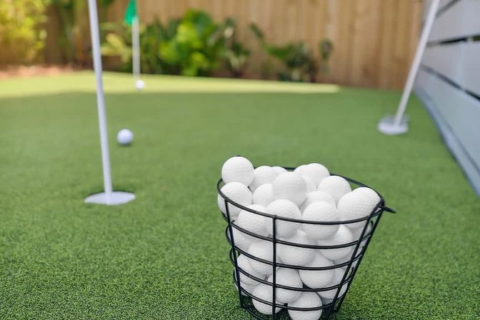 Black wire basket of white golf balls on a backyard putting green with practice flags and putting holes