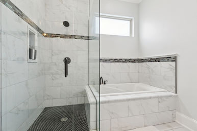 Sleek modern bathroom with glass-enclosed marble-tiled shower and black hexagon tile floor, built-in niche, adjacent marble-surrounded soaking tub, mosaic accent tile border, black matte fixtures and small frosted window
