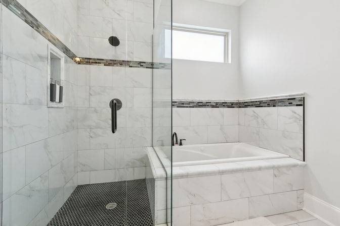 Sleek modern bathroom with glass-enclosed marble-tiled shower and black hexagon tile floor, built-in niche, adjacent marble-surrounded soaking tub, mosaic accent tile border, black matte fixtures and small frosted window