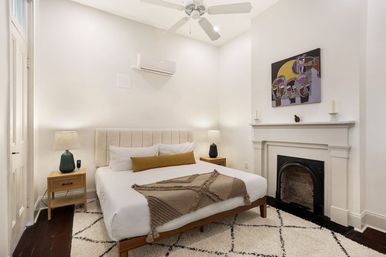Cozy modern urban apartment bedroom with queen bed, decorative fireplace, ceiling fan, abstract wall art and neutral linens