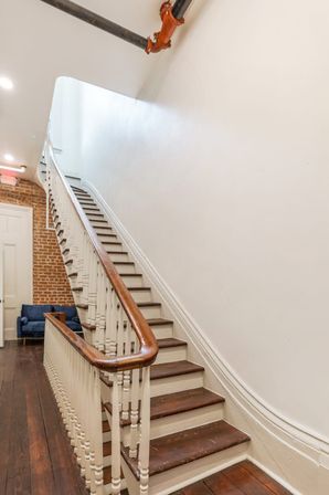 Cozy interior staircase in a historic townhouse: dark wooden steps, white balusters and curved wood handrail, exposed brick wall, hardwood floor and overhead pipe.