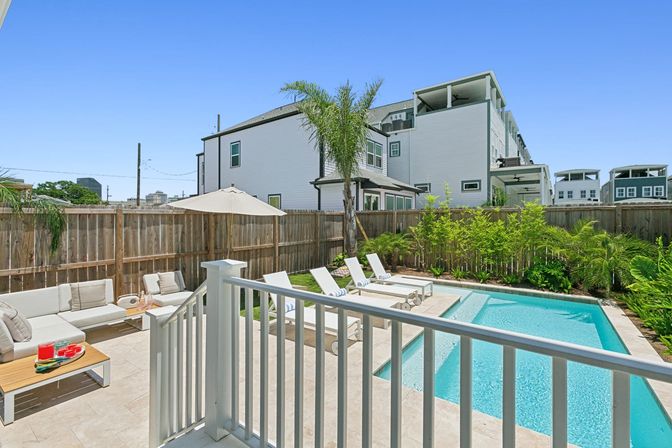 Sunny urban townhouse backyard with turquoise private pool, sun loungers, umbrella, patio sofa and palm tree