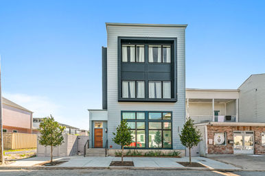 Contemporary three-story urban townhouse with black-framed windows, wood front door, young street trees and a bright blue sky.