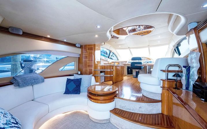 Luxurious yacht salon and helm with teak floors, curved white leather seating and panoramic windows at a marina