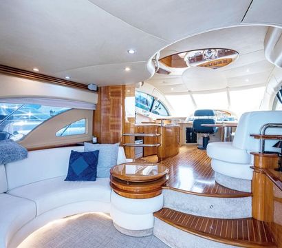 Luxurious yacht salon and helm with teak floors, curved white leather seating and panoramic windows at a marina