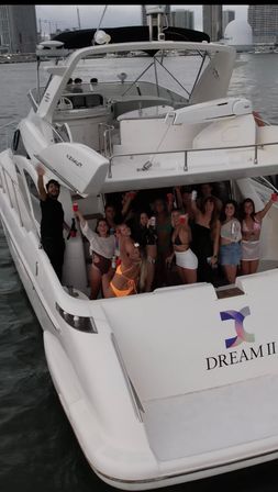 Lively group of people raising drinks on the aft deck of a white luxury yacht near an urban waterfront skyline at dusk — yacht party, boat cruise, harbor scene.