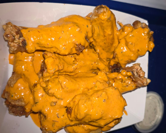 Crispy fried chicken wings smothered in bright orange buffalo sauce in a white takeout tray with a small cup of ranch dip visible