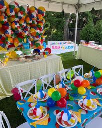 Colorful beach-ball themed kids' birthday setup in a backyard tent with a giant balloon wall, ball pit, decorated tables, playful centerpieces and cake.