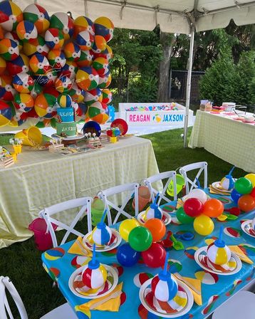 Colorful beach-ball themed kids' birthday setup in a backyard tent with a giant balloon wall, ball pit, decorated tables, playful centerpieces and cake.