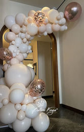 Cream and blush organic balloon garland with rose-gold confetti balloons framing an indoor arched doorway in a modern entryway