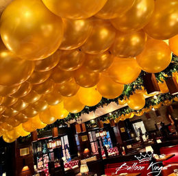 Festive indoor restaurant scene with ceiling packed with shiny gold balloons, holiday evergreen garlands, warm lighting, and cozy red booth seating.