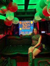 Smiling woman in knee-high boots poses in a neon-green lit party bus interior with balloons and a bright "Happy 30th Birthday" sign.