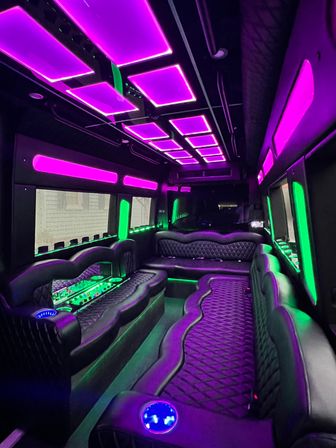 Party bus interior with quilted black leather wraparound seating, vibrant purple ceiling panels and green LED accent lighting, mirrored bar area and illuminated cup holders