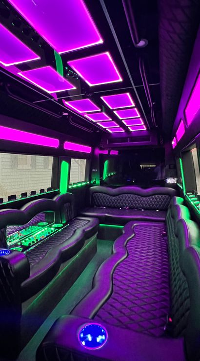 Party bus interior with quilted black leather wraparound seating, vibrant purple ceiling panels and green LED accent lighting, mirrored bar area and illuminated cup holders