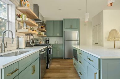 Bright modern kitchen with mint-green shaker cabinets, white quartz island, open wood shelves, stainless steel appliances and warm hardwood floors