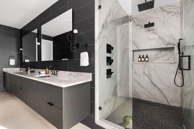 Modern spa-like bathroom with marble walk-in shower and glass enclosure, dark textured tile walls, double marble vanity, large mirrors and black matte fixtures.