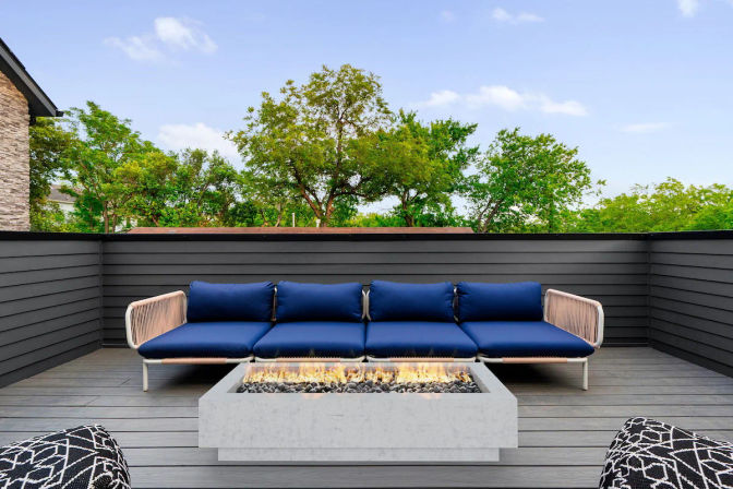 Modern rooftop patio deck with navy-cushioned sectional sofa and rectangular concrete fire pit overlooking leafy treetops