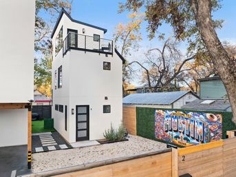 Contemporary three-story white micro‑home with rooftop deck, black trim and gravel courtyard, colorful 'Welcome to Austin, Texas' mural on the fence
