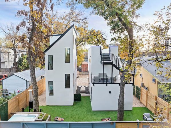 Sleek white modern townhouses on a narrow urban lot with exterior staircase and rooftop deck, artificial turf backyard with hot tub, mature trees and wooden fencing