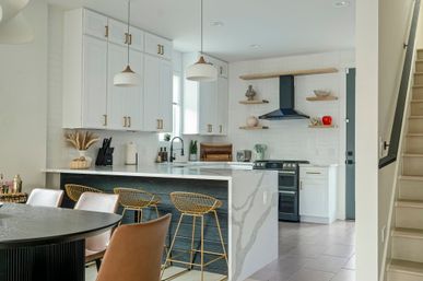 Bright modern kitchen with white shaker cabinets, marble waterfall island, gold wire bar stools, open wood shelves and black range hood