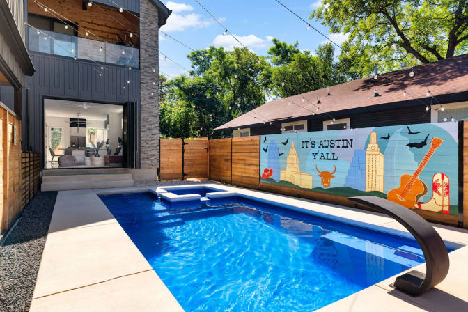 Modern Austin backyard with rectangular blue pool, built-in loungers and curved fountain, string lights overhead, and a colorful wooden mural reading "It's Austin Y'All" with guitar, cowboy boot and skyline