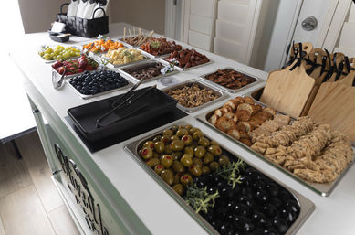 Self-serve charcuterie buffet on white island with trays of green and black olives, assorted crackers and crostini, blueberries, strawberries, grapes, cubed cheeses, nuts, pretzels and cured meats — stylish catered appetizer spread