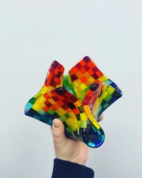 Hand holding a wavy, handmade fused glass bowl with a vibrant rainbow checkerboard mosaic pattern