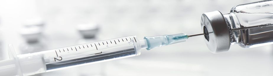 Close-up of a syringe drawing clear vaccine from a glass vial in a clinical setting, ready for injection